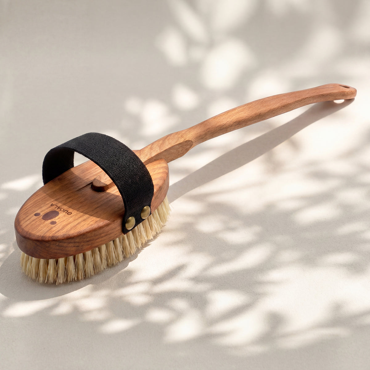 Badebürste schräg von oben: schwarzes Halteband mit zwei Nieten und QUOALA-Logo im Holz
